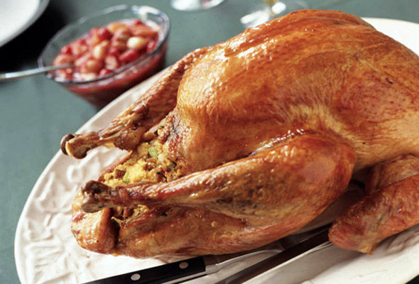 A cooked turkey filled with bread stuffing with bacon, apples, sage, and caramelized onions on a white platter.