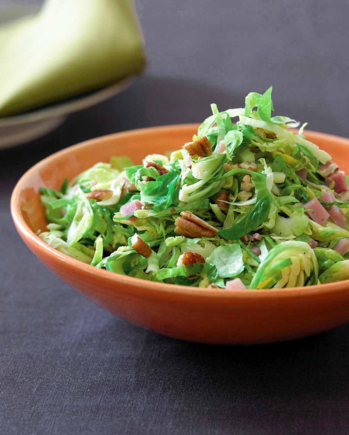 An orange bowl filled with sauteed Brussels sprouts, ham, and toasted pecans.