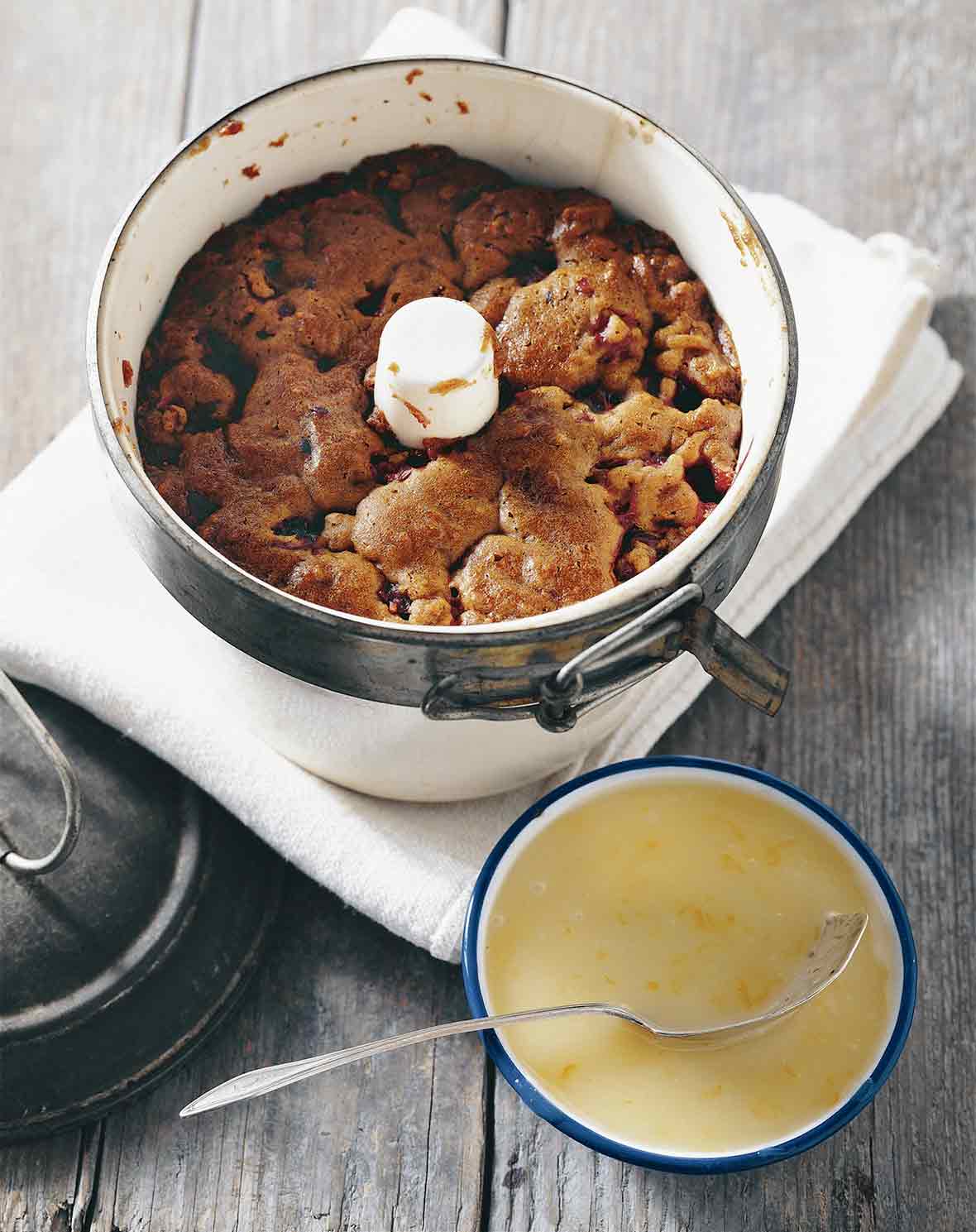Steamed cranberry pudding in a tube pan on a napkin with a bowl of butter-orange sauce