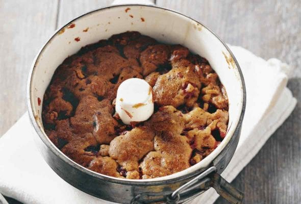 Steamed cranberry pudding in a tube pan on a napkin with a bowl of butter-orange sauce.