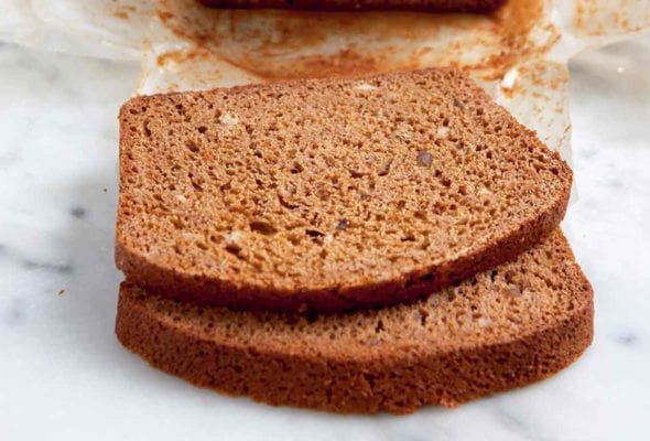 A loaf of Burgundian honey spice bread on a sheet of parchment with two slices cut off.