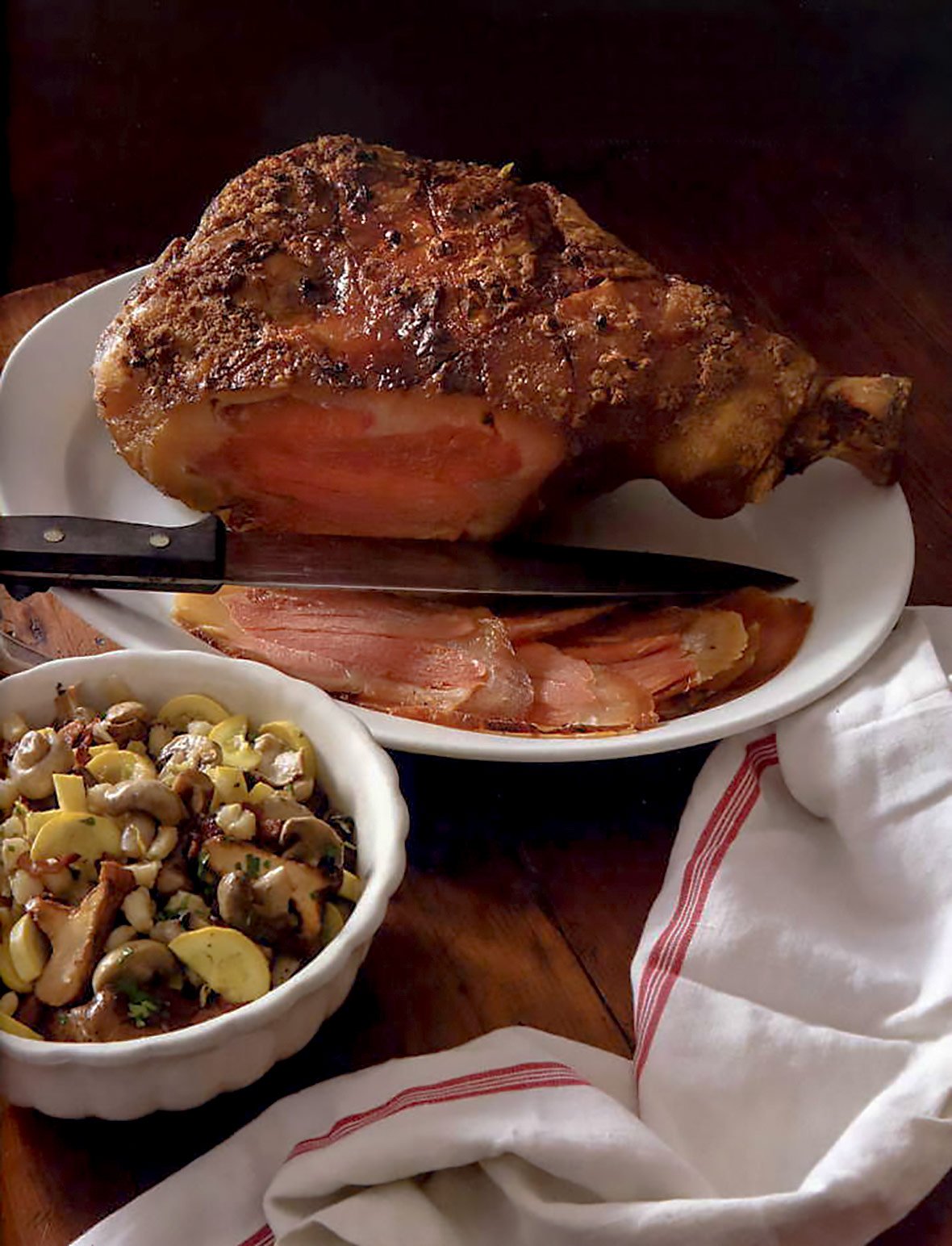 A baked country ham on an oval platter with a knife resting beside it.