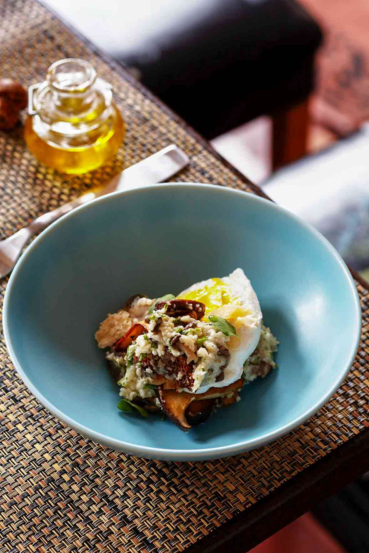 Blue bowl of wild mushroom grits topped with an egg, parmesan cheese, and basil