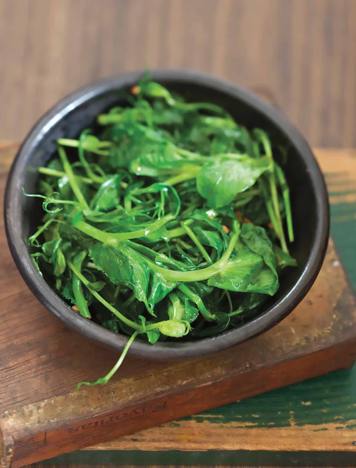 A brown bowl filled with stir-fried pea shoots