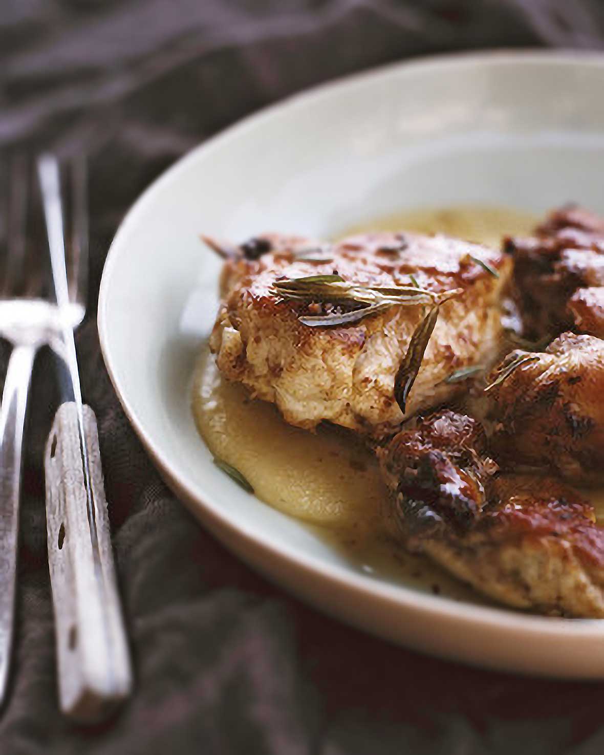 Chicken pieces in a sauce of vinegar, garlic, rosemary in a white plate, knife and fork on the side