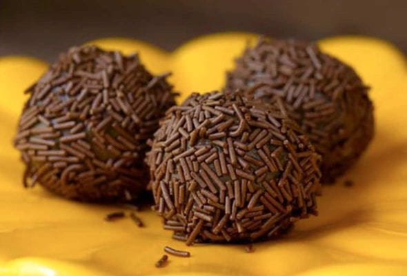 Three golf-ball size chocolate Brazilian candies covered with chocolate sprinkles on a yellow plate