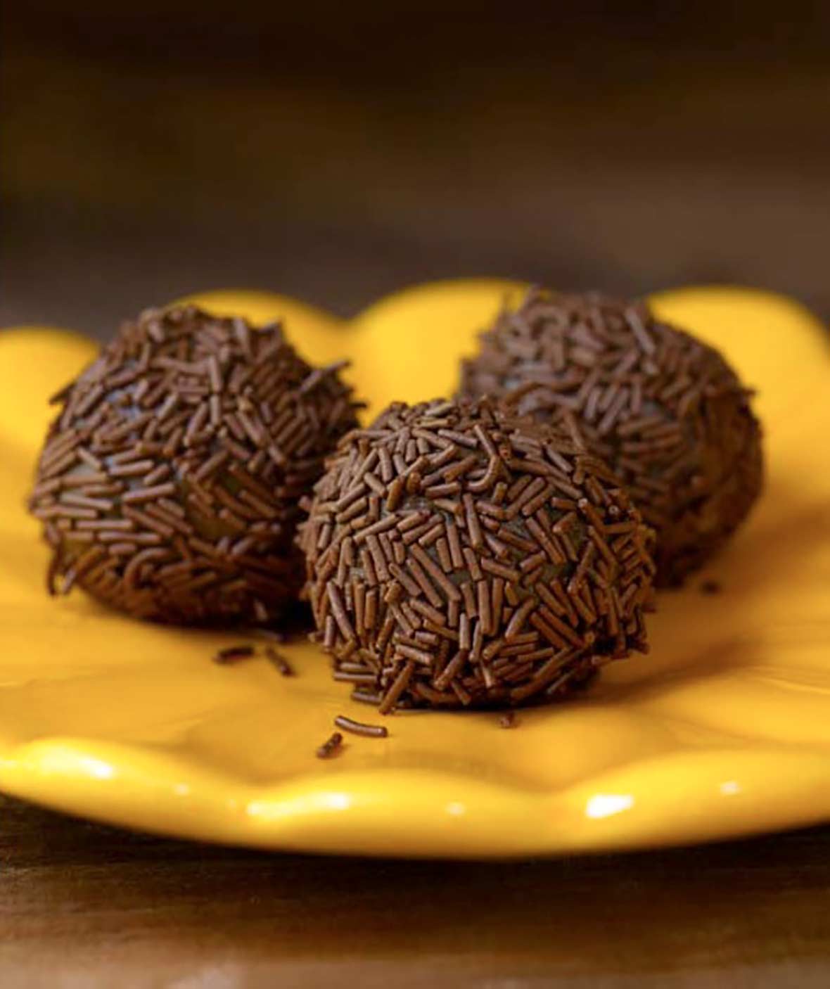 Three golf-ball size chocolate Brazilian candies covered with chocolate sprinkles on a yellow plate