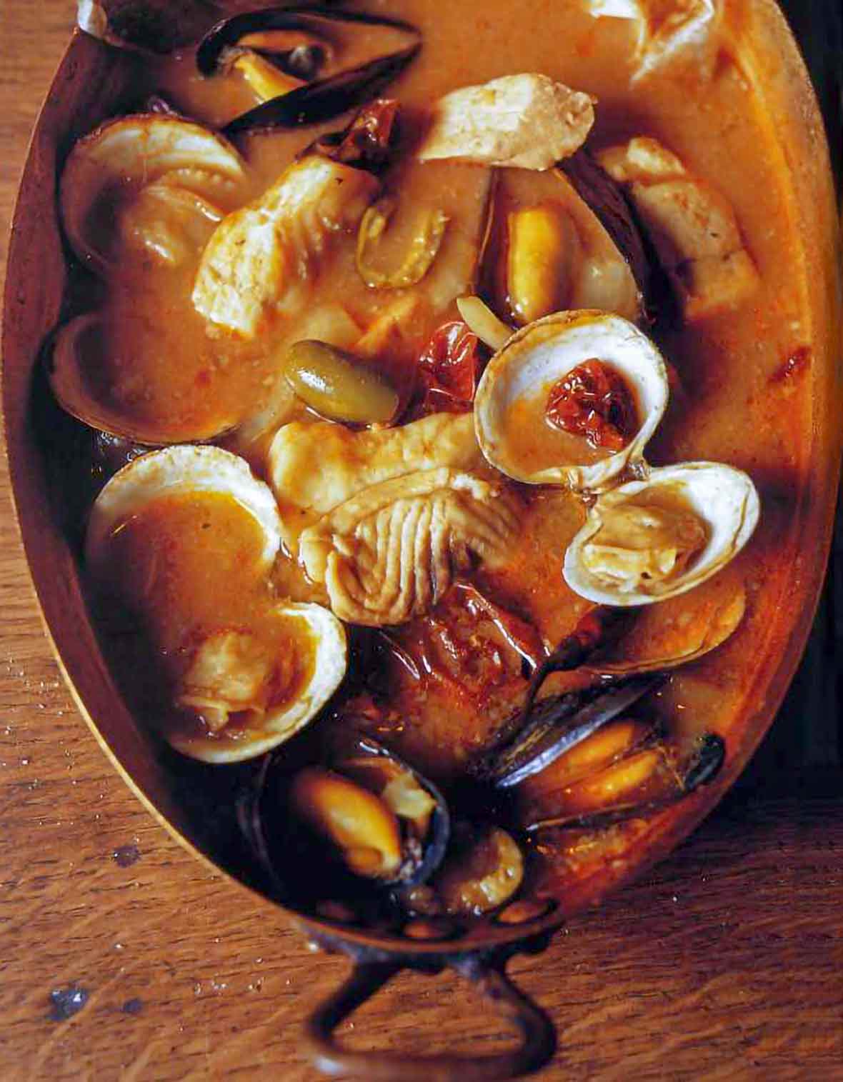 Copper pot with seafood soup with fish fillets, clams, mussels, olives, tomato broth