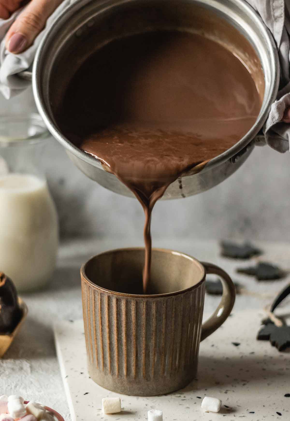 Hot chocolate to suit any taste being poured from a metal saucepan into a mug.
