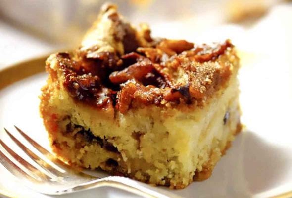 A square of Passover apple cake on a stack of plates with a fork resting beside it and the remainder of the cake in the background.