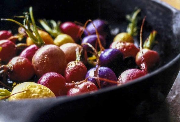Black skillet with red, white, yellow, and purple roasted radishes