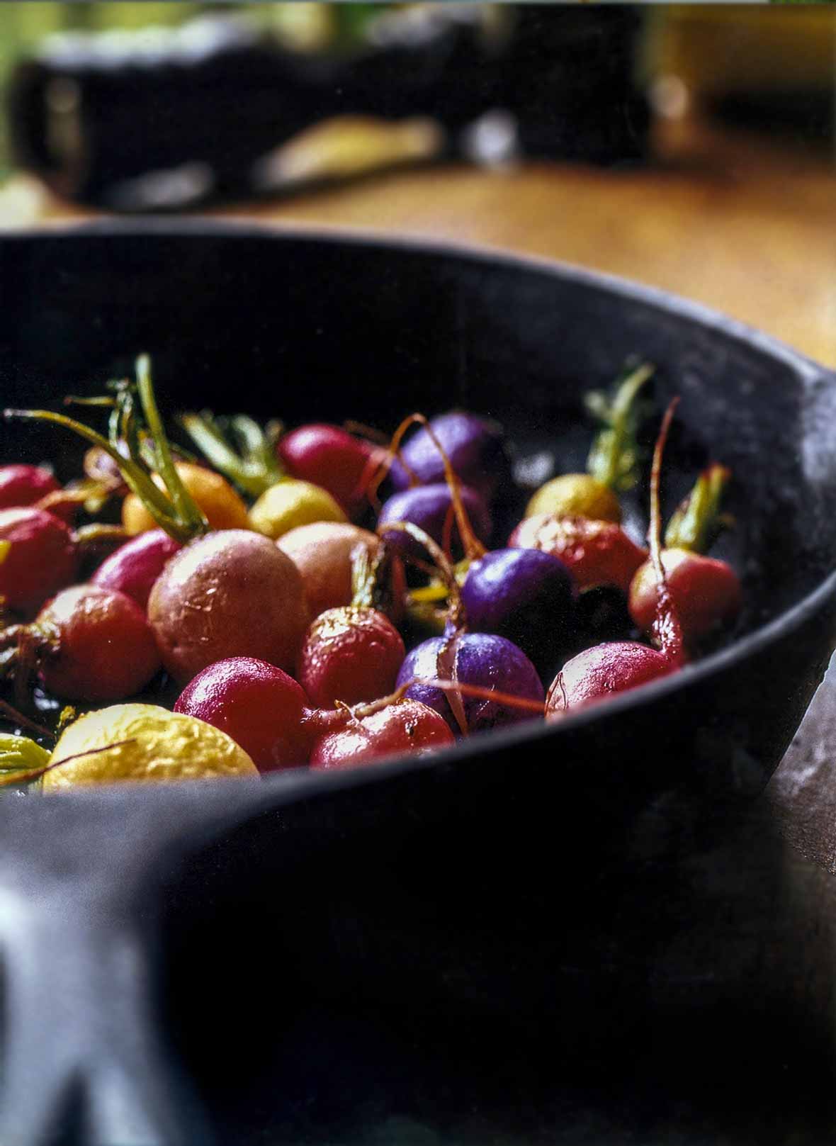 Black skillet with red, white, yellow, and purple roasted radishes