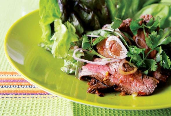 A green plate topped with a grilled Thai beef salad made with lettuce, beef, shallots, and cilantro.