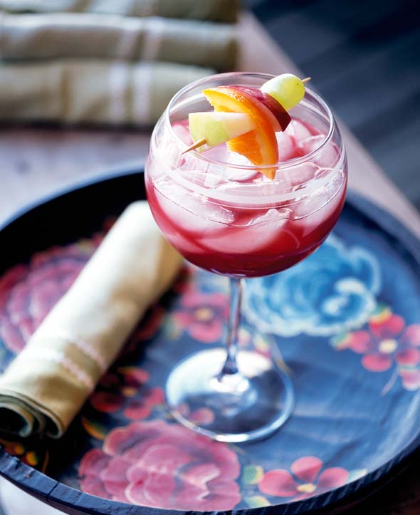 A wine glass filled with ruby sangria, ice, and a fruit skewer on a floral-patterned serving tray.