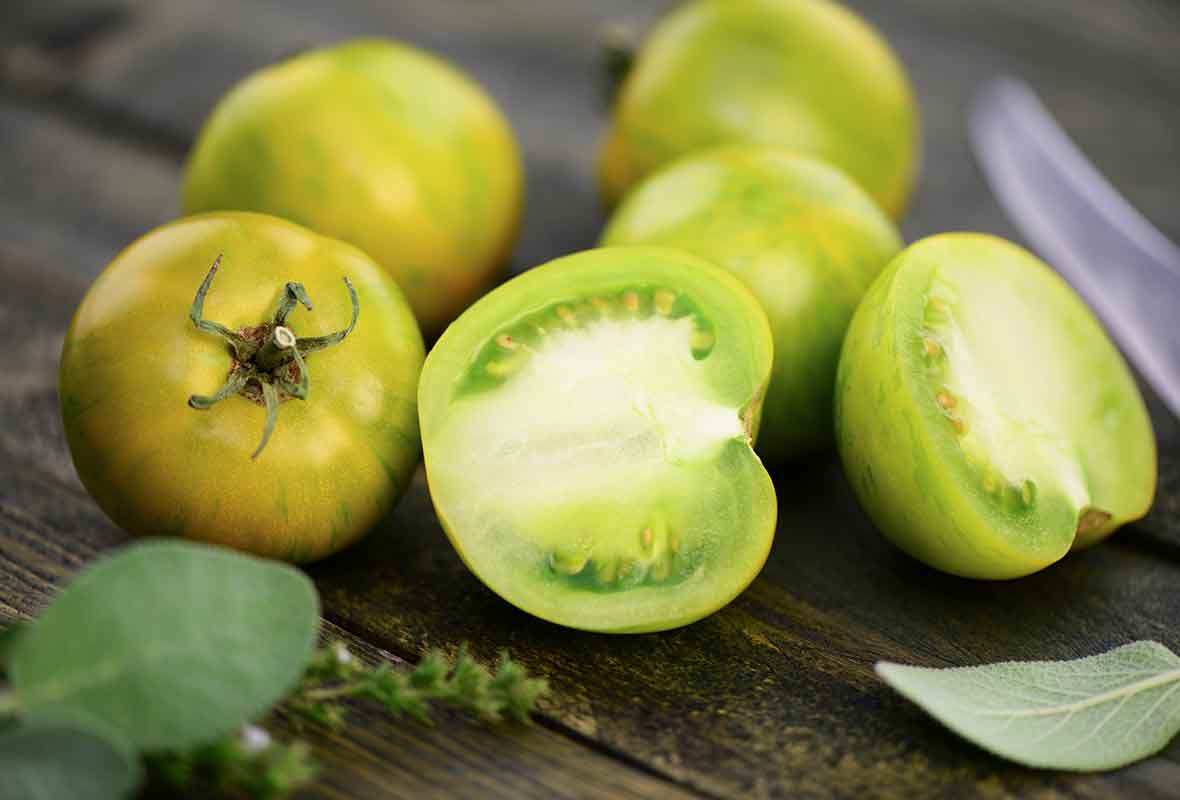 Four whole and one halved green tomato with a sprig of thyme and a couple of sage leaves to be used in the corn and green tomato salad.