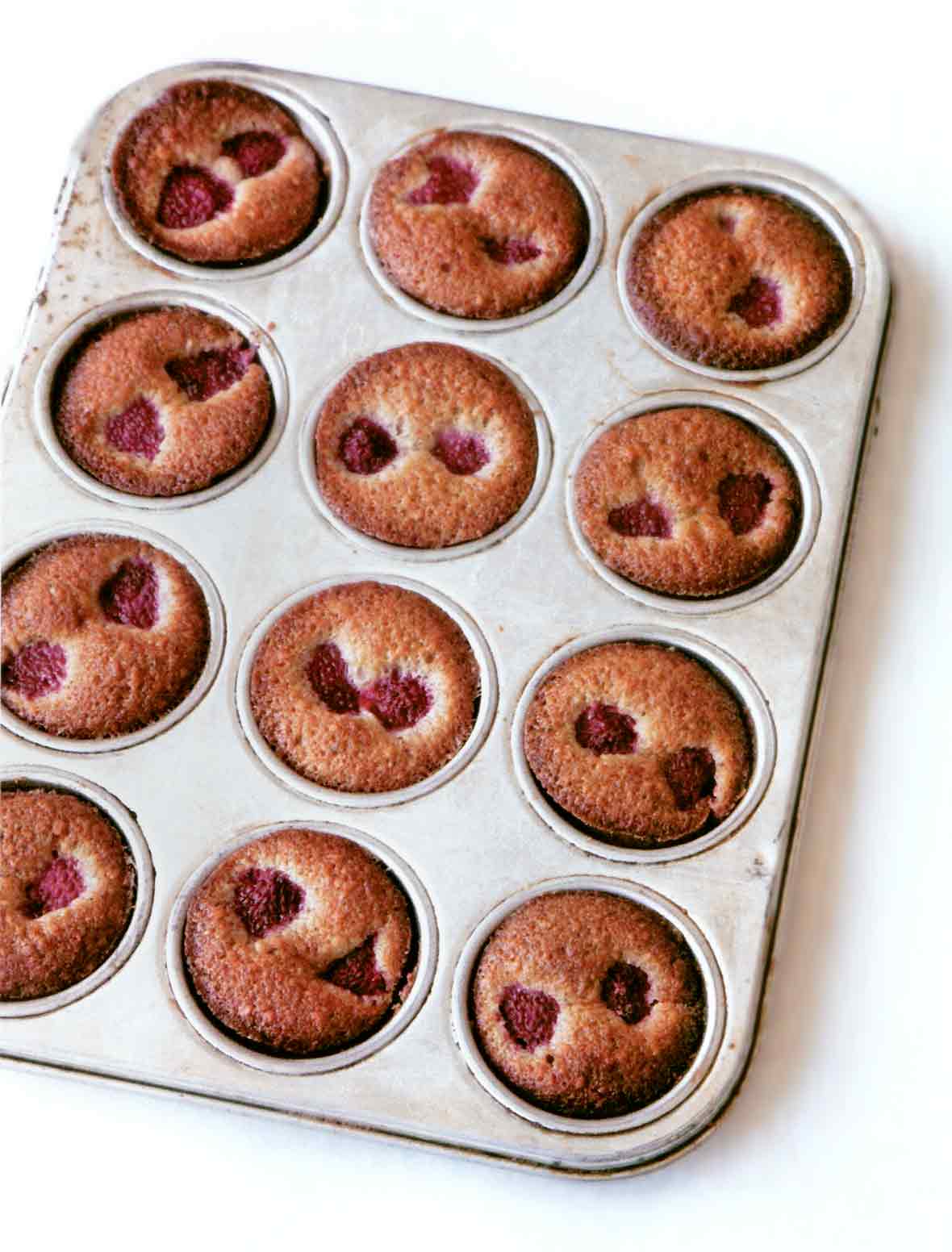 Muffin tin filled with 12 mini-muffin financiers studded with raspberries