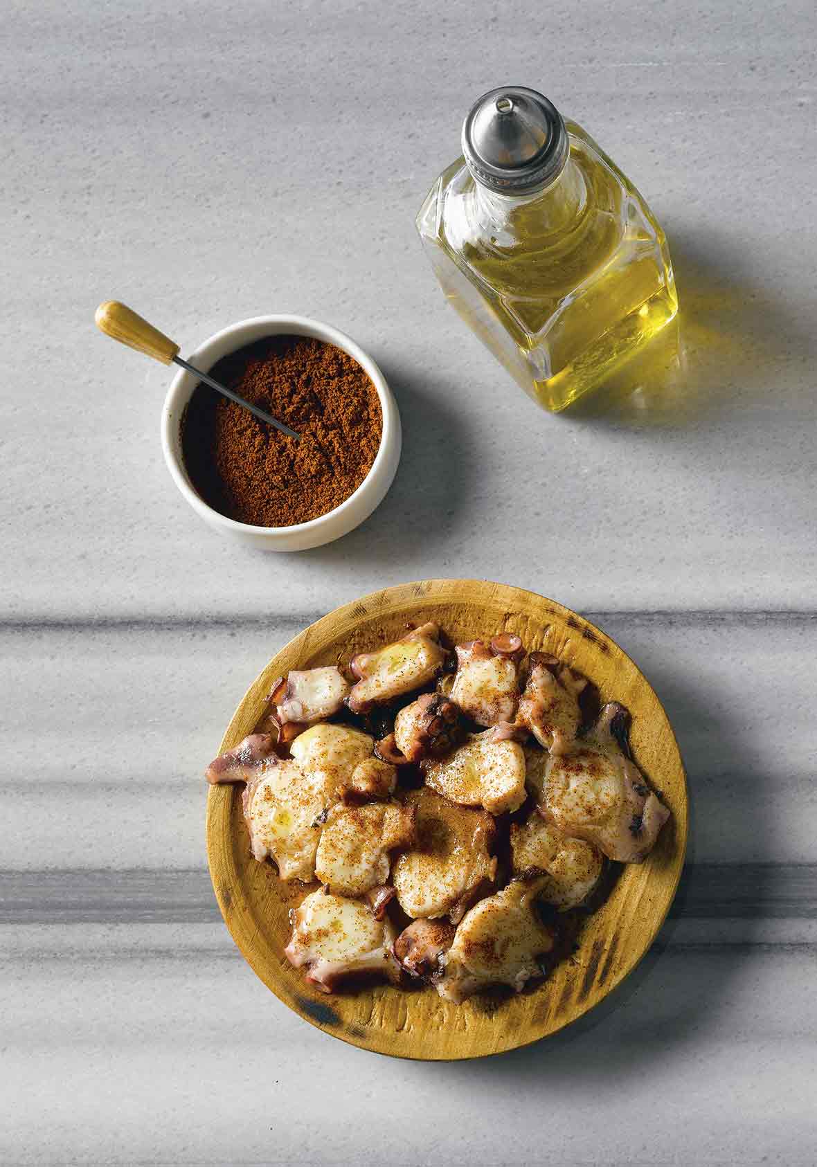 Wooden bowl of octopus with paprika, bowl of paprika, cruet of olive oil