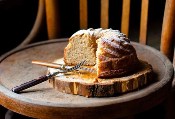 A partially cut St. Phanourios cake on a wooden slab on a wooden chair.