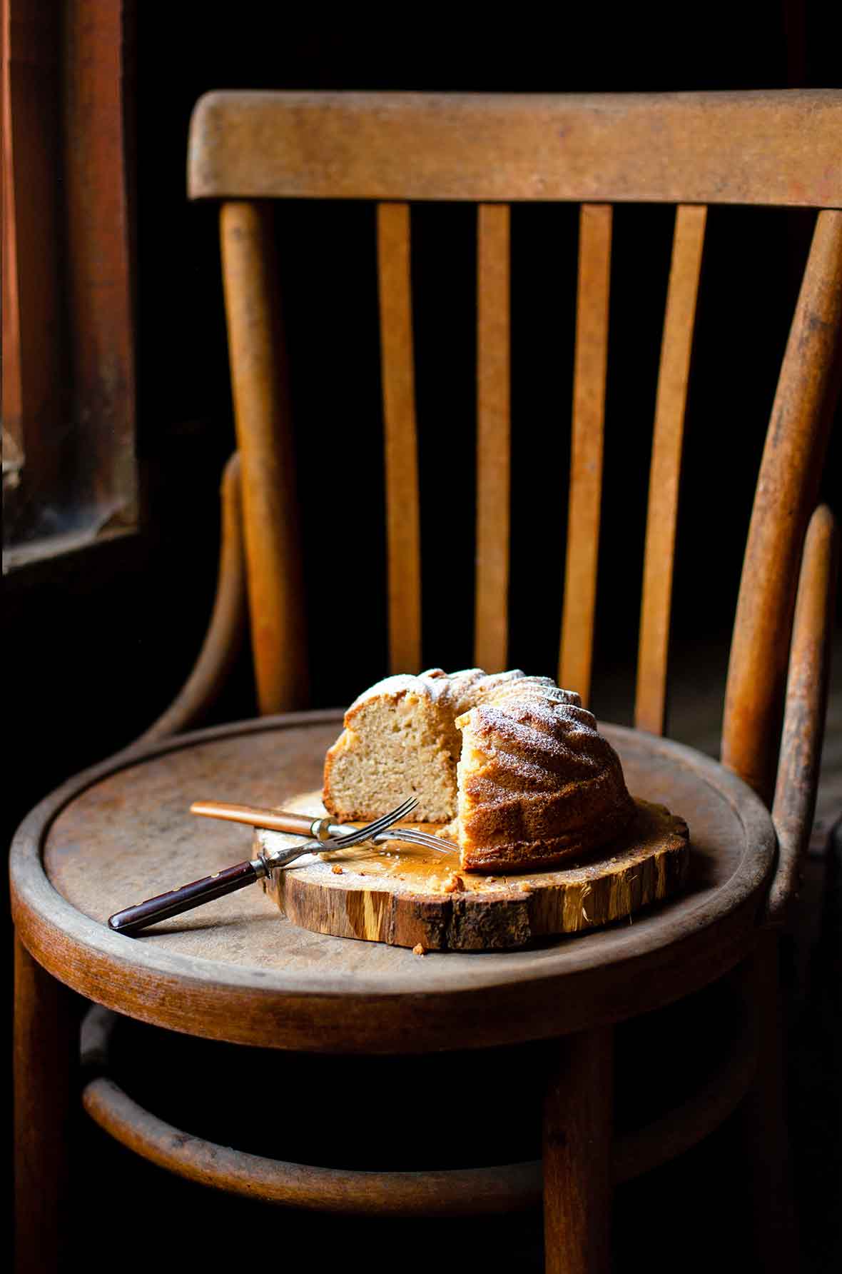 A partially cut St. Phanourios cake on a wooden slab on a wooden chair.