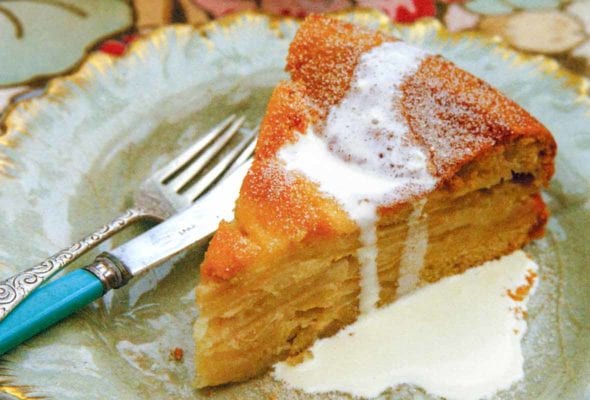A decorative plate topped with a slice of drunken apple cake that is drizzled with cream.