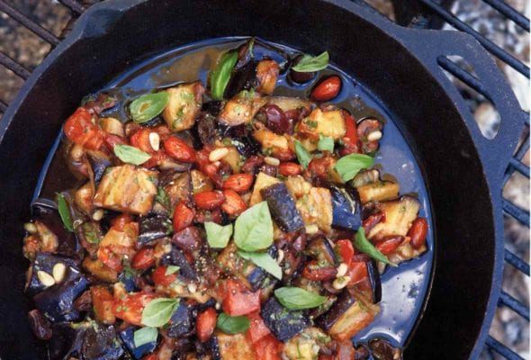 Skillet on a grill filled with eggplant caponata--chopped eggplant, onions, fennel, onions, almonds, basil