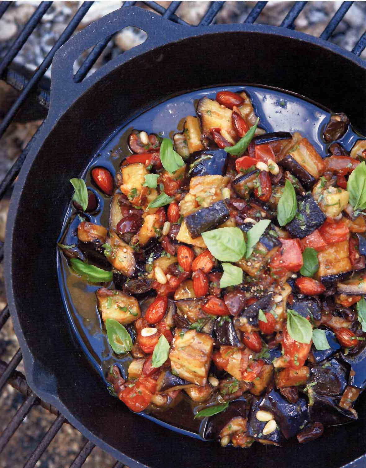 Skillet on a grill filled with eggplant caponata--chopped eggplant, onions, fennel, onions, almonds, basil