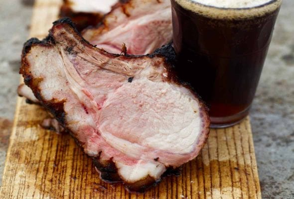 Chops from a spice-glazed grilled pork loin on a cutting board with a glass of stout.
