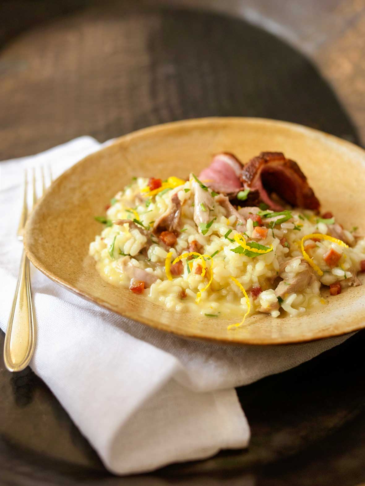 A wide ceramic bowl filled with Portuguese duck risotto, topped with orange zest and parsley.
