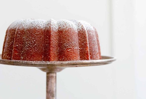 A Portuguese orange olive oil cake, dusted with confectioners' sugar on a silver cake stand.