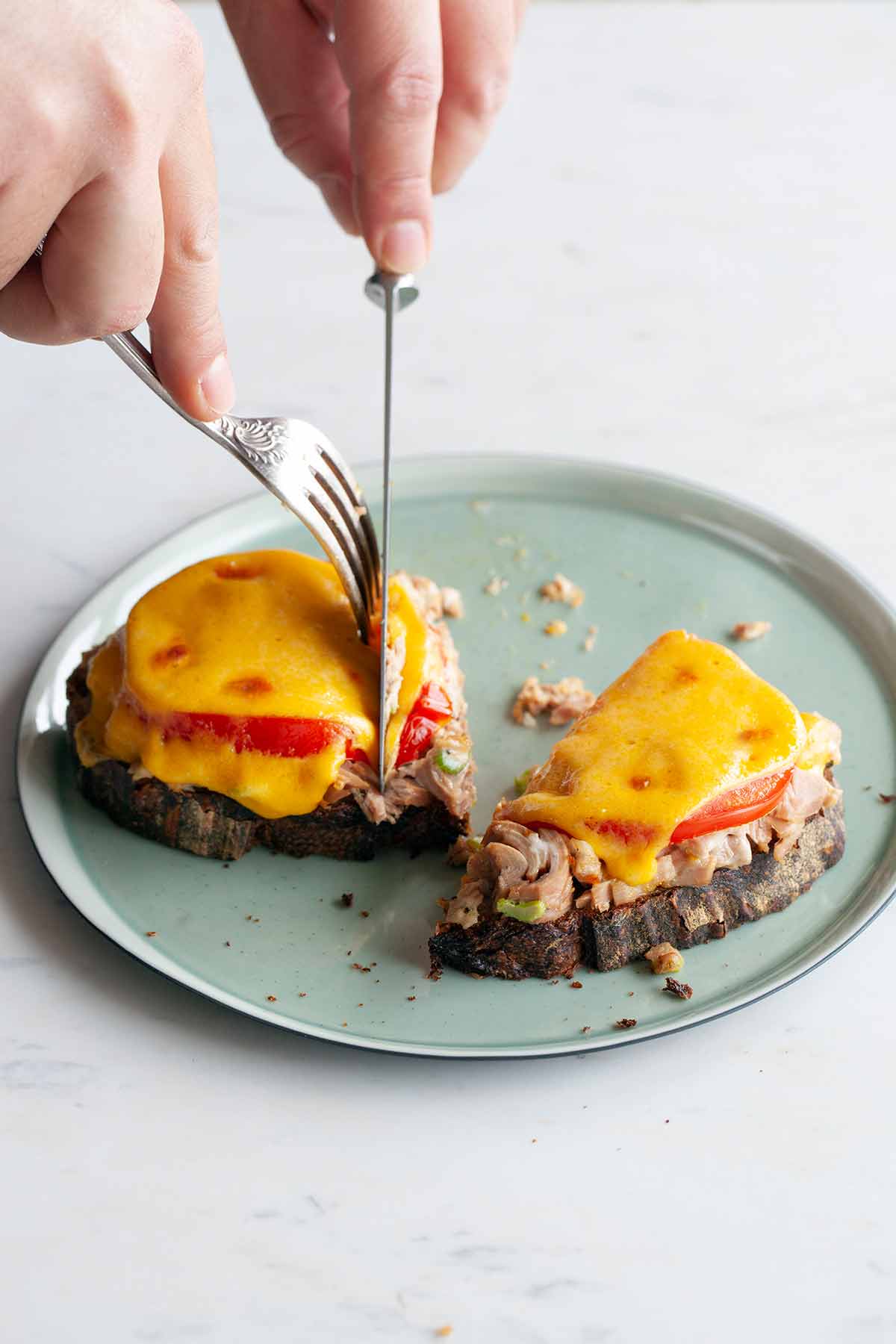 A person cutting into a halved tuna melt.