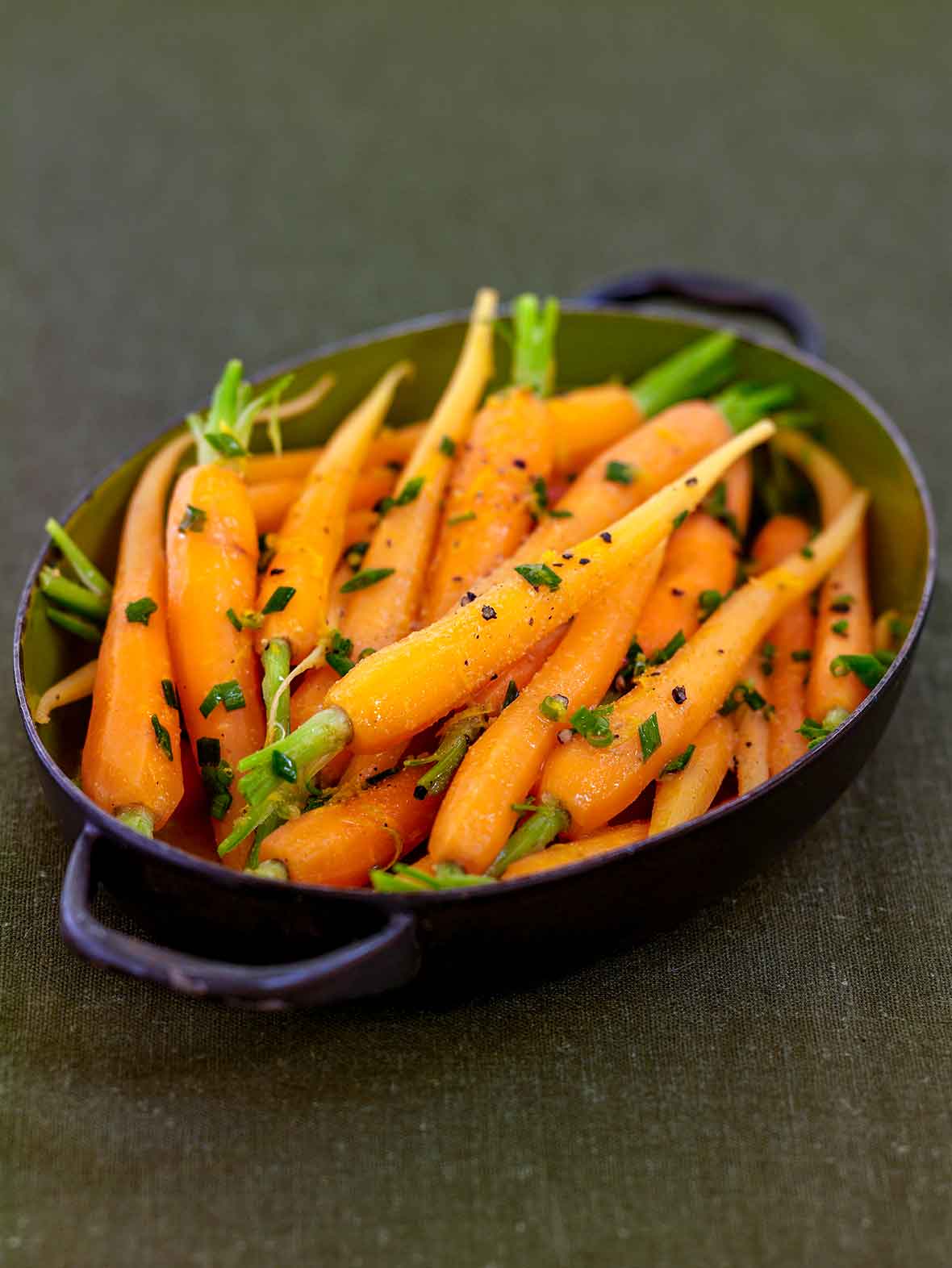 Oval pan with cumin-scented carrots sprinkled with chopped chives, orange zest, and pepper