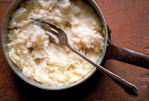 A pot of fork-mashed potatoes with a fork resting inside.