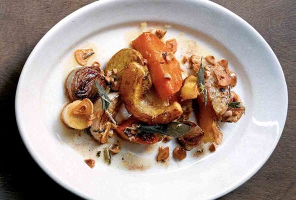 A white oval platter filled with roasted root vegetables and Marcona almonds, drizzled with sage-garlic brown butter.
