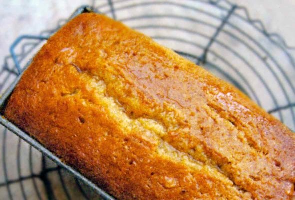 Glazed nutmeg pound cake in a loaf pan on a circular cooling rack