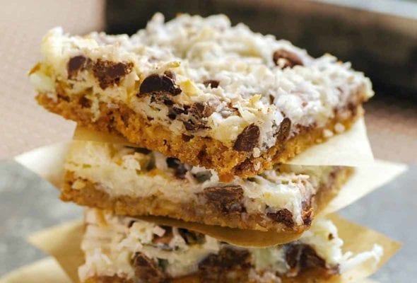Stack of four bars made of coconut, chocolate, graham crackers, each on a square of paper