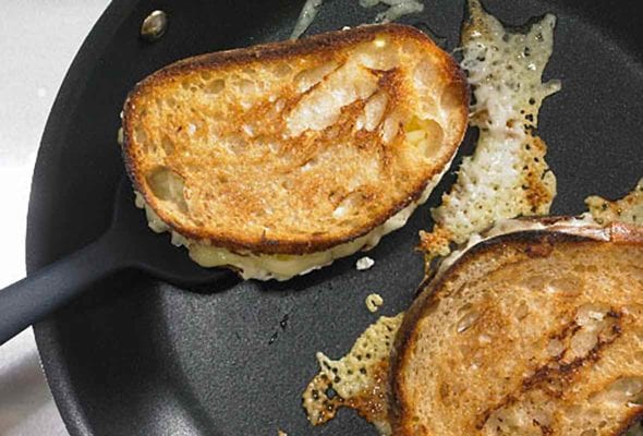 Two Hog Island grilled cheese sandwiches in a skillet with a spatula under one.