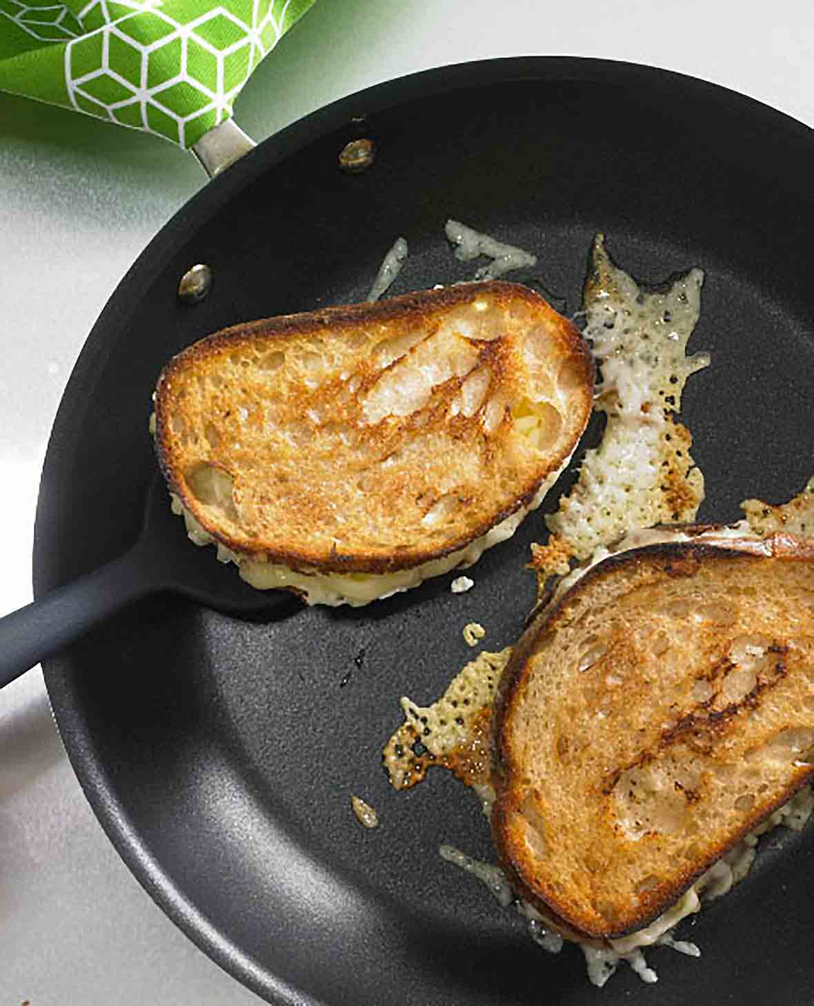 Two Hog Island grilled cheese sandwiches in a skillet with a spatula under one.