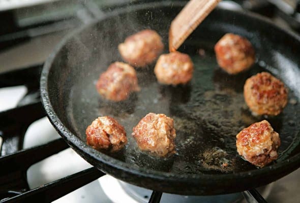 A cast-iron skillet with eight cheater's chorizo meatballs being cooked in it.