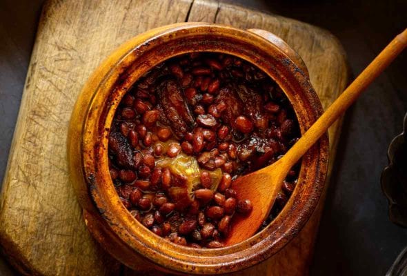 A bean pot of baked beans with a wooden spoon placed on a wooden chair