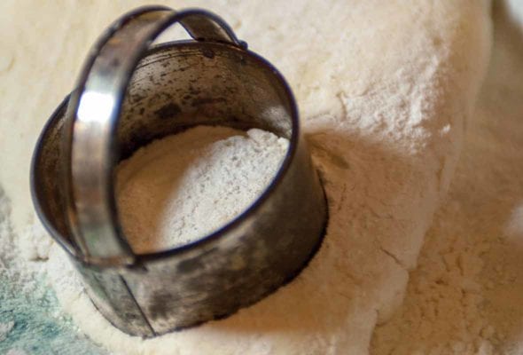 A woman's hand using a biscuit cutter on cream biscuit dough