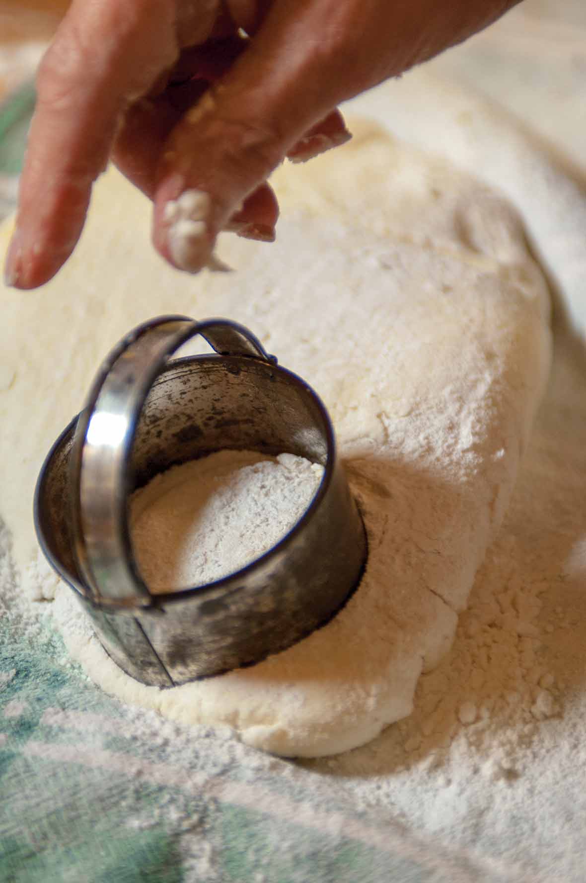 A woman's hand using a biscuit cutter on cream biscuit dough