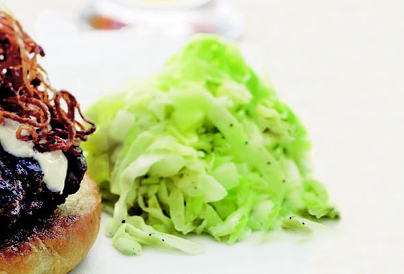 A pile of creamy coleslaw next to a burger topped with fried onions.