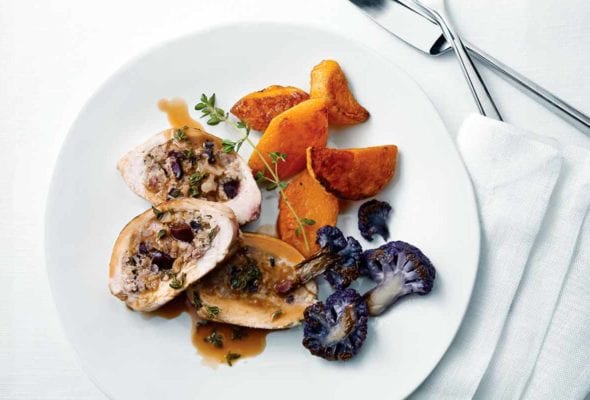 A sliced Mediterranean-style stuffed chicken breast on a white plate with purple cauliflower, sweet potato, and a sprig of thyme.