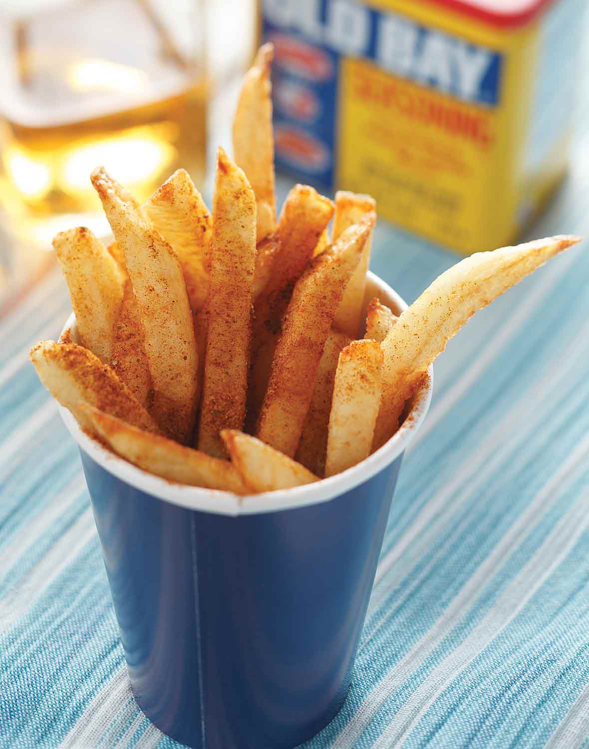 A blue paper cup filled with beach fries that are sprinkled with Old Bay seasoning.