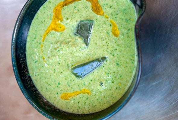Black bowl of green gazpacho, with two ice cubes, drizzle of olive oil
