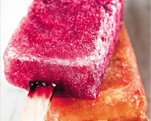 A hibiscus ice pop lying on top of a spicy mango ice pop.