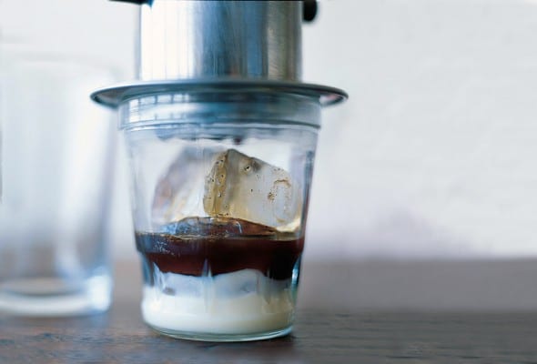 A glass of Vietnamese iced coffee, made with layers of sweetened condensed milk, coffee, and ice cubes with a coffee drip over it.