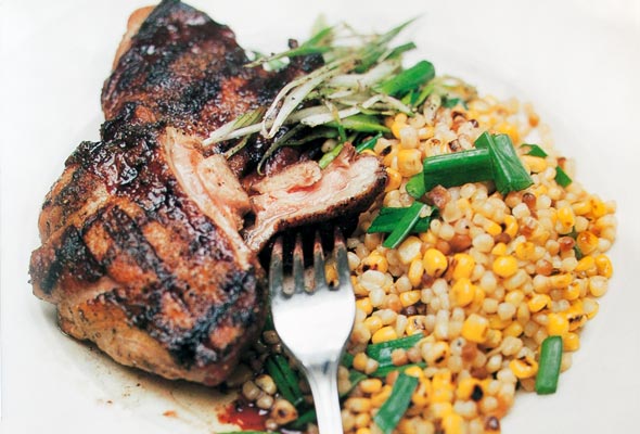 A piece of grilled guinea hen with sweet corn fregula beside it, all topped with chopped scallions.
