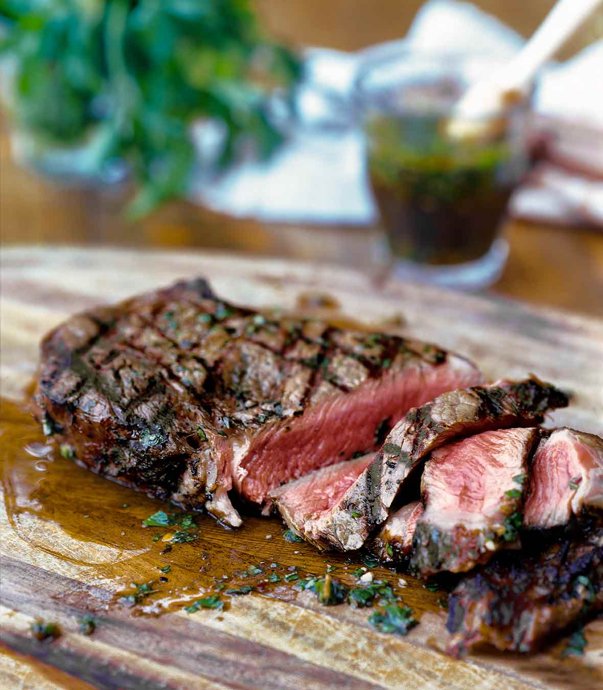 A sliced steak with chimichurri sauce drizzled on top on a cutting board