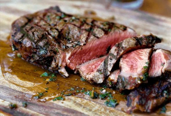 A sliced steak with chimichurri sauce drizzled on top on a cutting board